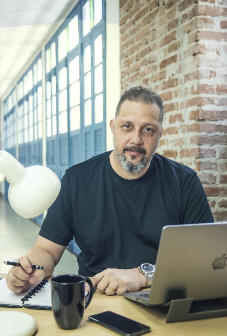 Luciano Passaretti trabalhando no notebook, com caderno de anotações e café na mesa